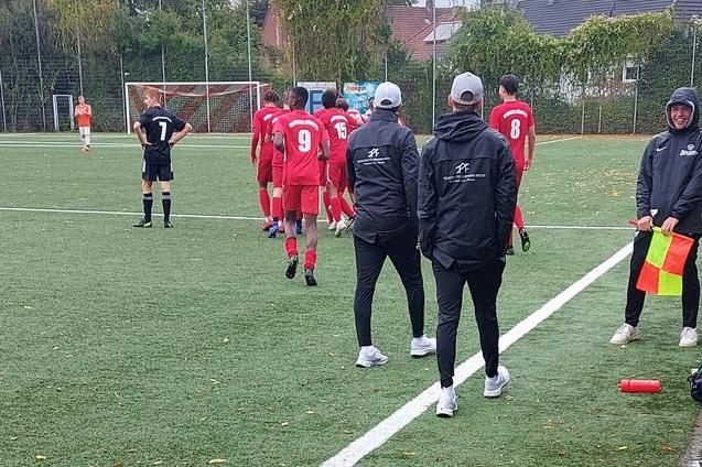 Fu&szlig;ballspieler in roten Trikots betreten das Spielfeld, w&auml;hrend Trainer und Schiedsrichter am Rand stehen.