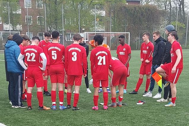 Gruppe junger Fu&szlig;ballspieler in roten Trikots versammelt sich auf dem Platz f&uuml;r eine Besprechung.