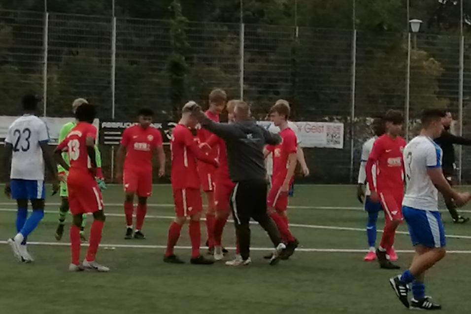 Gruppierung von Fu&szlig;ballspielern in roten Trikots auf dem Feld, w&auml;hrend ein Schiedsrichter die Situation beobachtet.