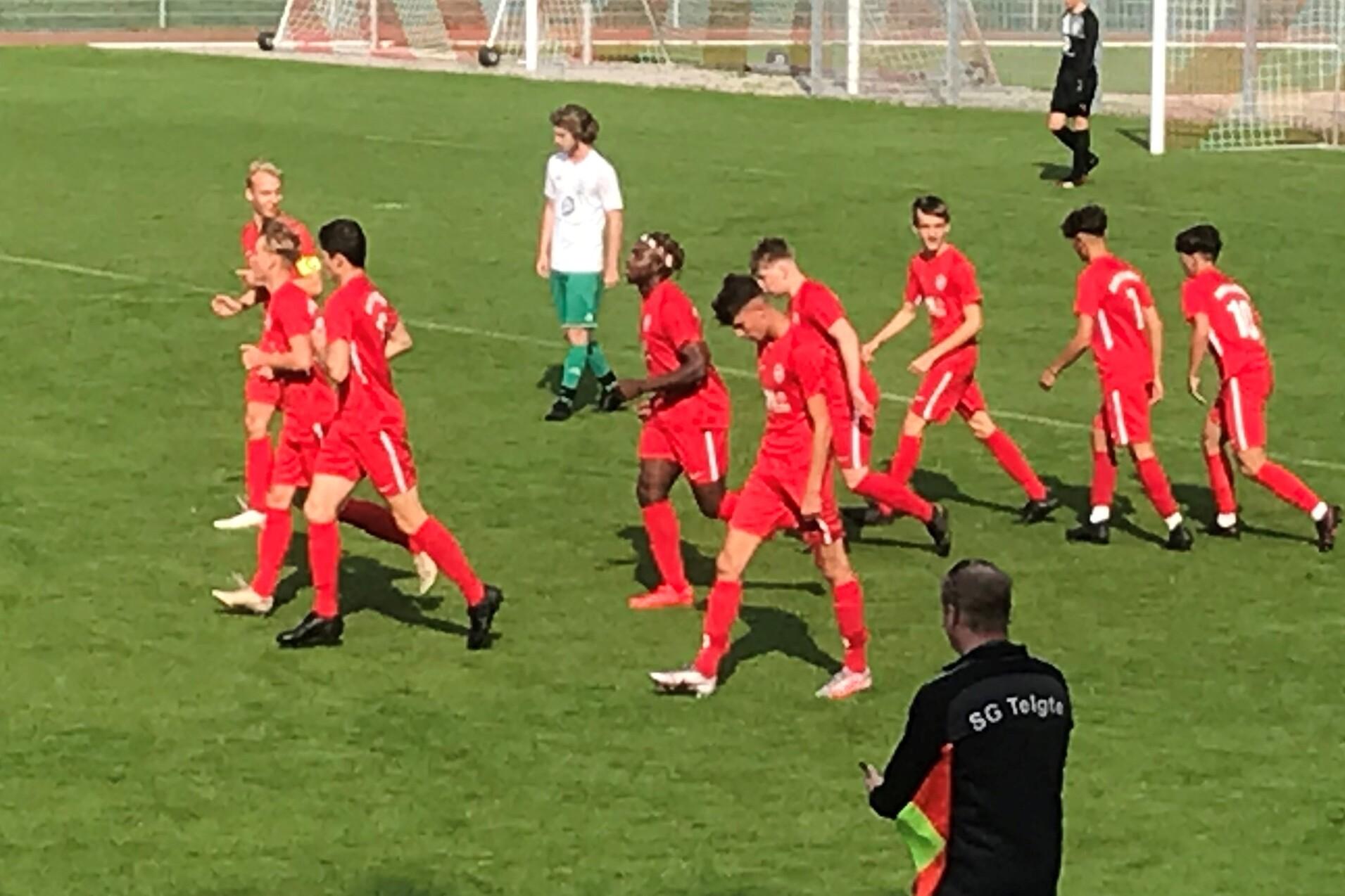 Fu&szlig;ballmannschaft in roten Trikots feiert einen Treffer auf dem Spielfeld mit Toren im Hintergrund.