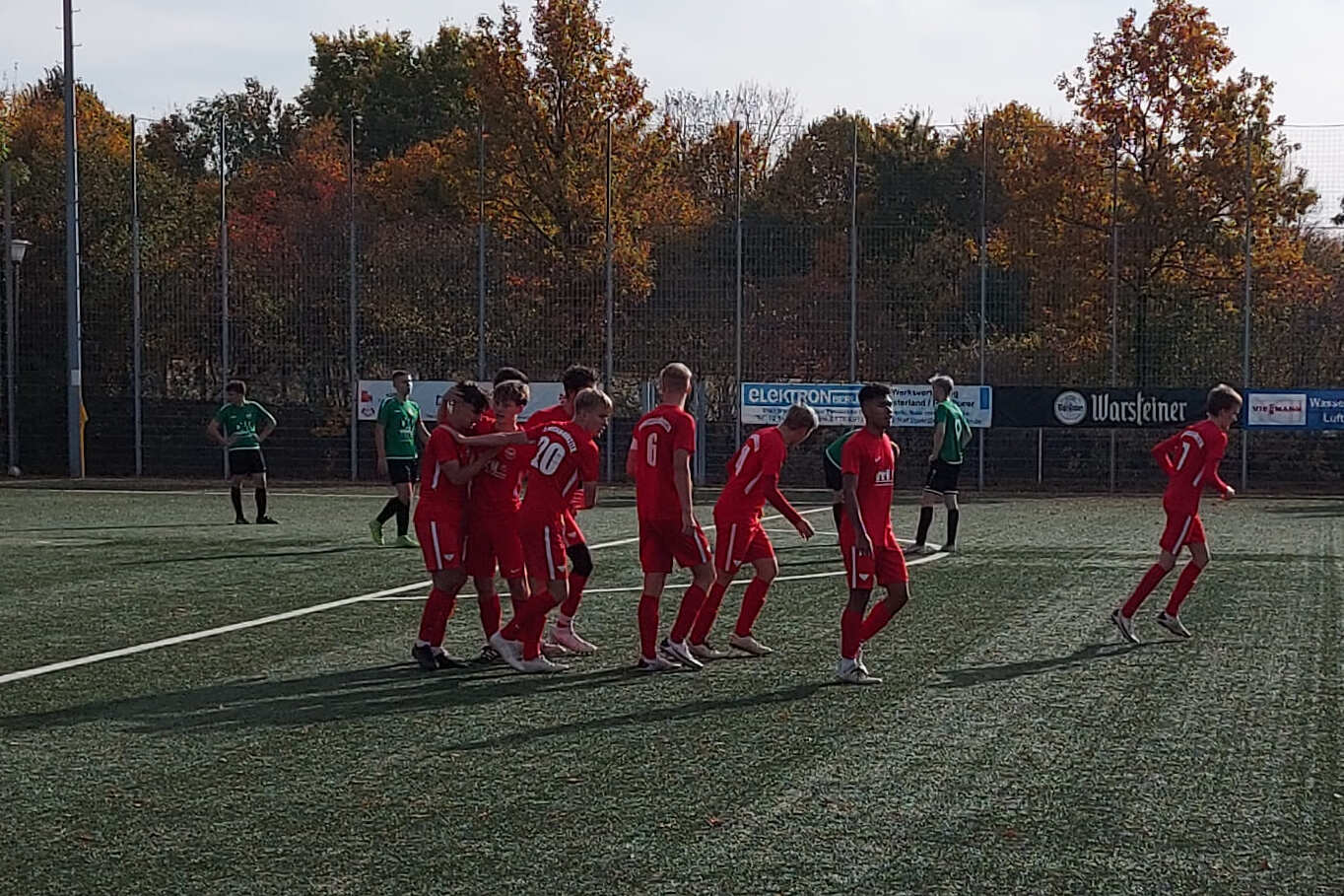 Eine Gruppe von Spielern in roten Trikots jubelt auf einem Fu&szlig;ballplatz im Freien zu einem unver&auml;nderten Spiel.