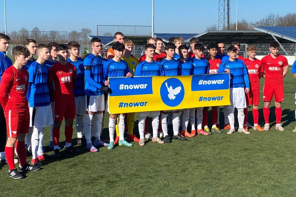 Gruppenbild von Fu&szlig;ballspielern in blauen und roten Trikots, die ein Banner mit der Aufschrift "#nowar" halten.