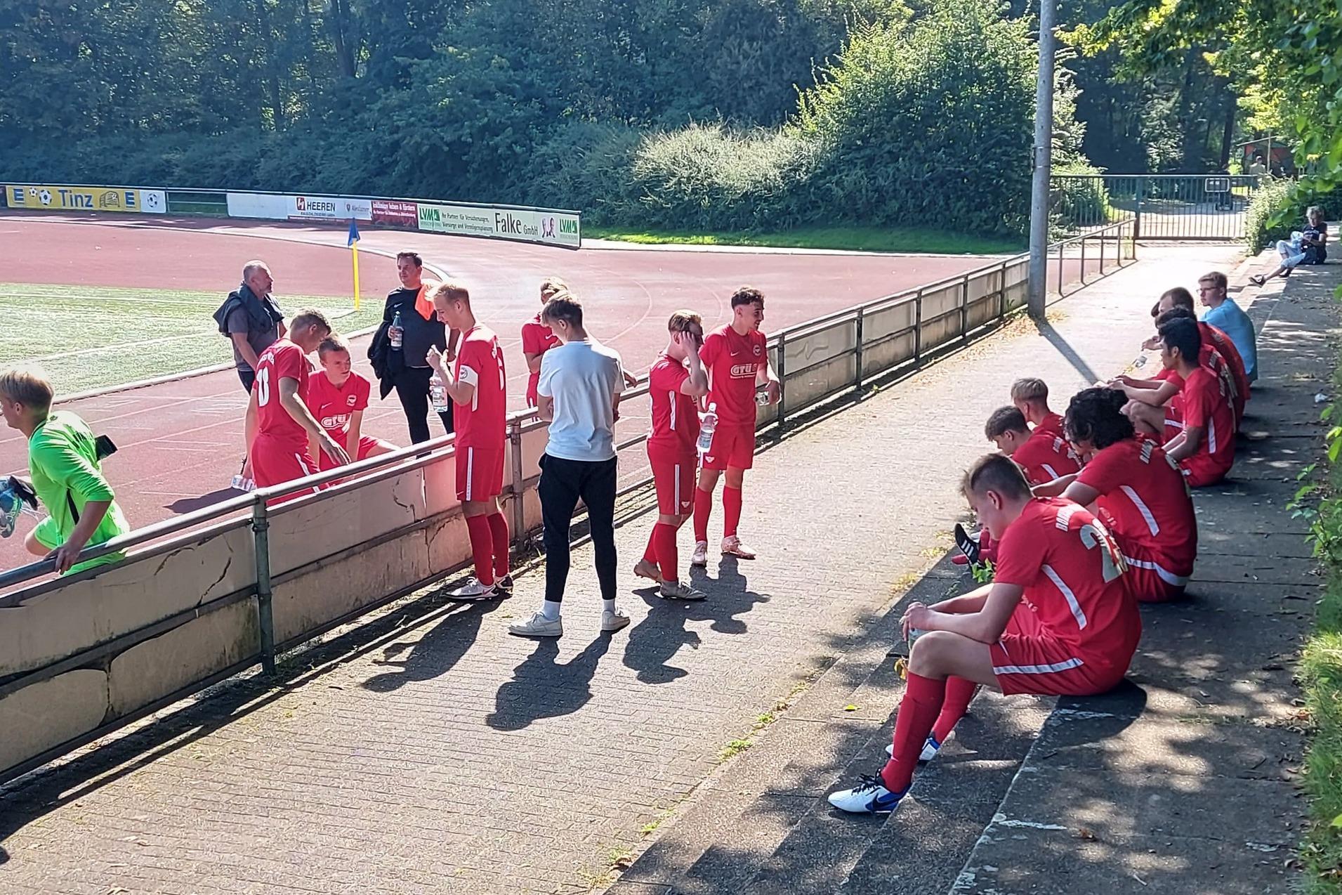 Gruppe von Fu&szlig;ballspielern in roten Trikots sitzt und steht am Spielfeldrand eines Sportgel&auml;ndes.