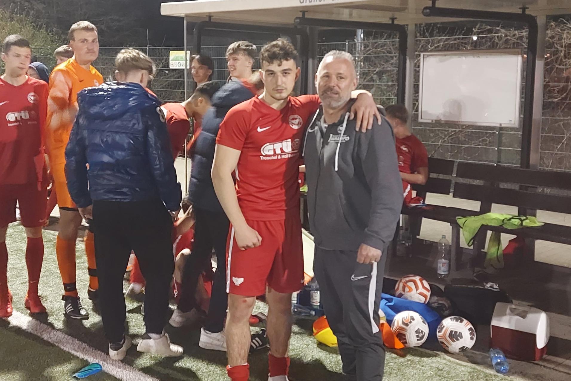 Gruppe von Fu&szlig;ballspielern in roten Trikots und Betreuern am Spielfeldrand bei Nacht. Mannschaftsbank im Hintergrund.