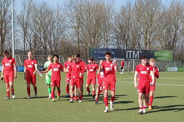 Gruppe von Spielern in roten Trikots, die auf einem Fu&szlig;ballplatz mit Kunstrasen zusammenl&auml;uft.