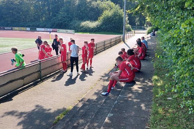 Gruppe von Fu&szlig;ballspielern in roten Trikots sitzt und steht am Spielfeldrand eines Sportgel&auml;ndes.