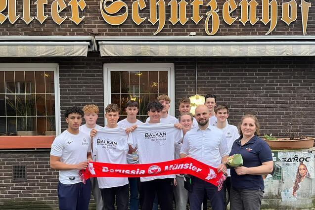 Gruppe von acht Personen vor dem "Alten Schutzenzhof", einige halten ein Schal von Borussia M&uuml;nster.
