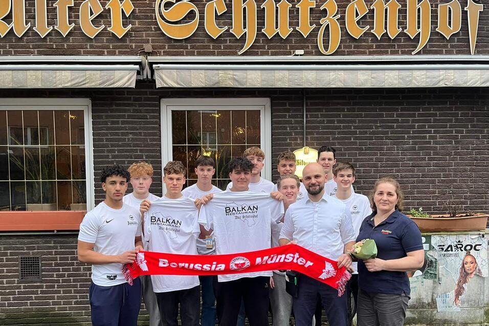 Gruppe von acht Personen vor dem "Alten Schutzenzhof", einige halten ein Schal von Borussia M&uuml;nster.