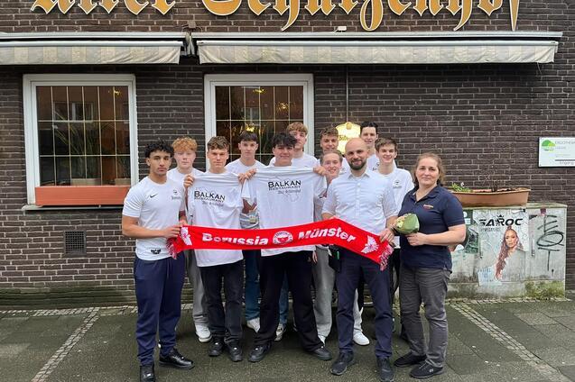 Gruppe von acht Personen vor dem "Alten Schutzenzhof", einige halten ein Schal von Borussia M&uuml;nster.