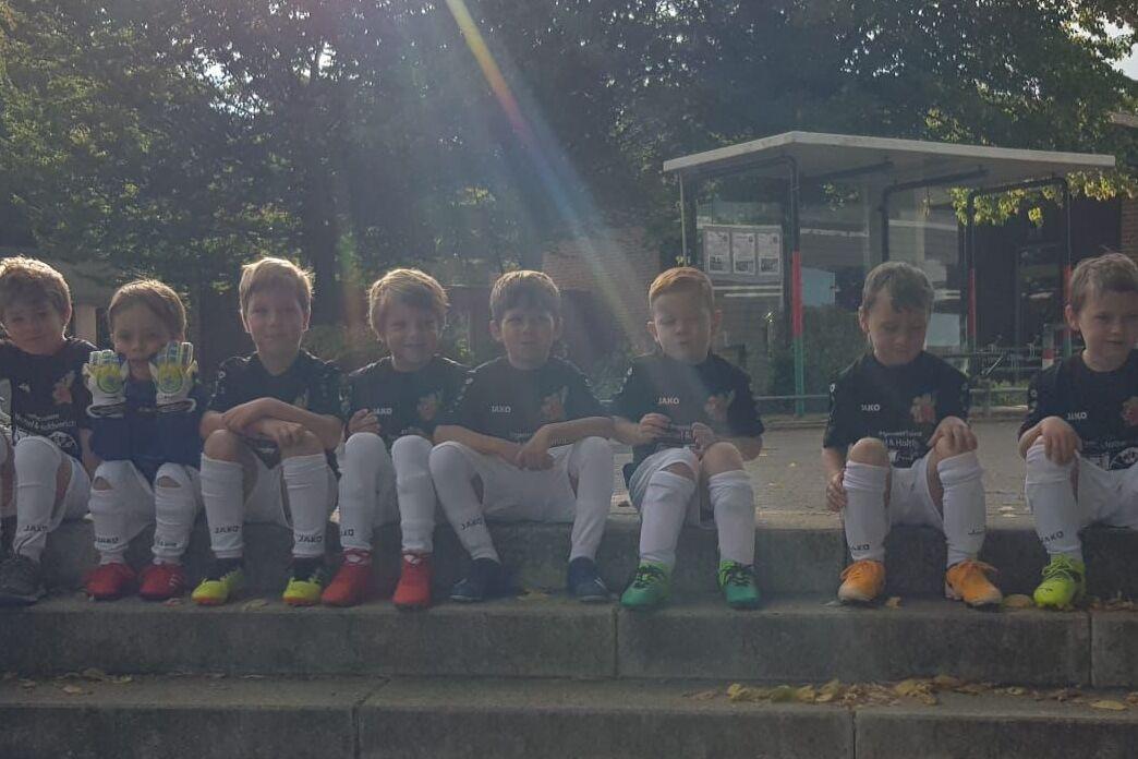 Gruppe von Kindern im Sportoutfit sitzt auf Treppenstufen in einem Au&szlig;enbereich, mit B&auml;umen im Hintergrund.