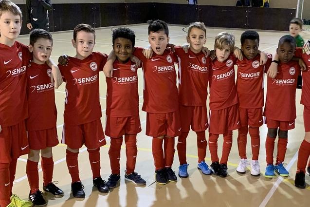 Gruppe von Kindern in roten Fu&szlig;balltrikots, die zusammen auf einem Sportplatz stehen, inklusive einem Torwart in Gr&uuml;n.
