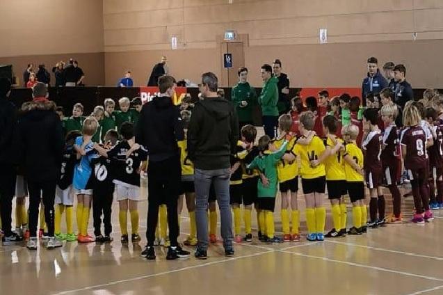 Zwei Gruppen von Kindern in Sportkleidung stehen in einem Kreis und halten sich w&auml;hrend eines Fu&szlig;ballevents die H&auml;nde.