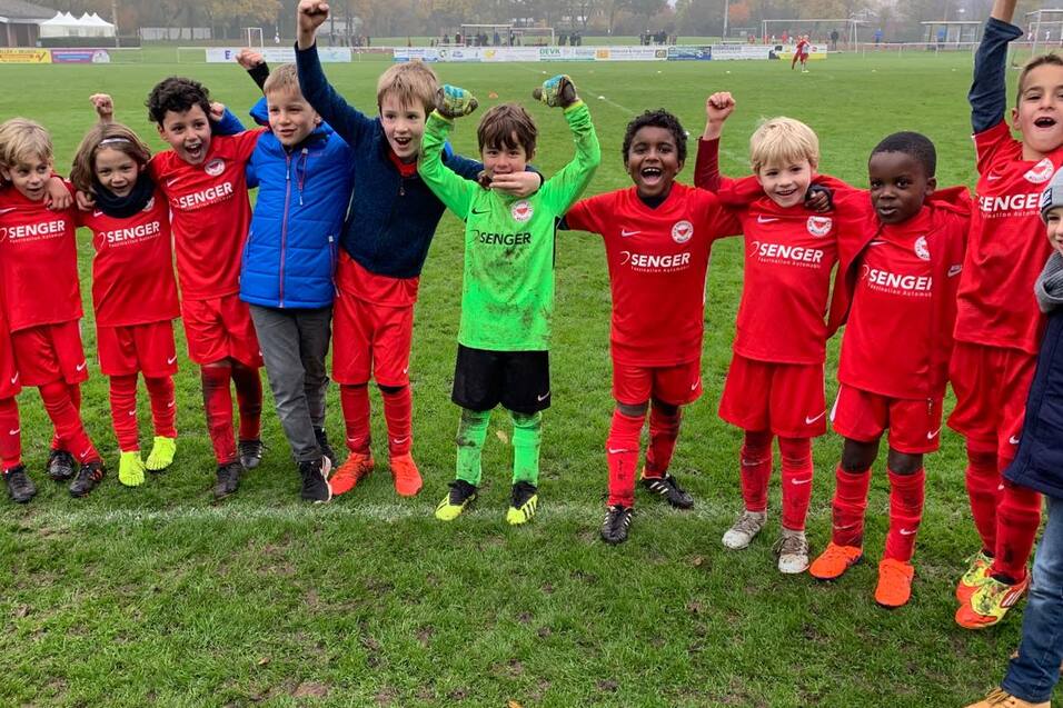 Gruppe von Kindern in roten Fu&szlig;balltrikots jubelt fr&ouml;hlich auf einem Sportfeld nach dem Spiel.