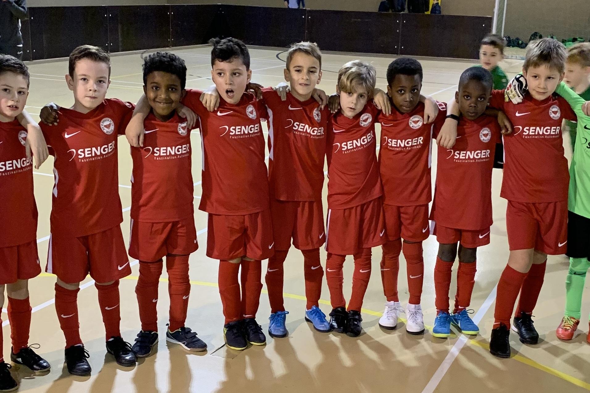 Gruppe von Kindern in roten Fu&szlig;balltrikots, die zusammen auf einem Sportplatz stehen, inklusive einem Torwart in Gr&uuml;n.