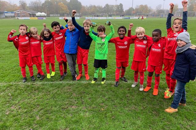 Gruppe von Kindern in roten Fu&szlig;balltrikots jubelt fr&ouml;hlich auf einem Sportfeld nach dem Spiel.
