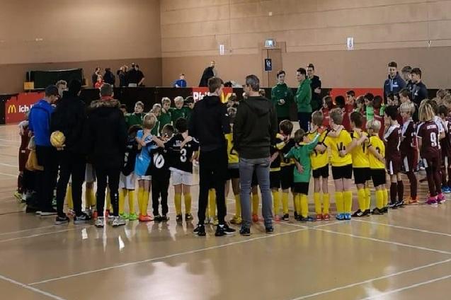 Zwei Gruppen von Kindern in Sportkleidung stehen in einem Kreis und halten sich w&auml;hrend eines Fu&szlig;ballevents die H&auml;nde.