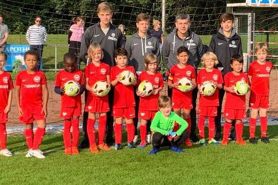 Gruppe von Fu&szlig;ballspielern in roten Trikots steht vor einem Tor, umgeben von einem Sportplatz und Zuschauern.