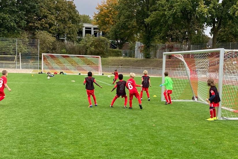 Gruppe von Kindern in roten Trikots beim Fu&szlig;ballspiel vor zwei Toren auf einem Rasenplatz.
