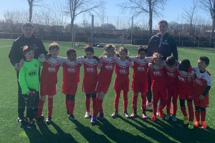 Eine Gruppe von elf jungen Fu&szlig;ballspielern in roten Trikots posiert auf einem Rasenplatz mit zwei Trainern.