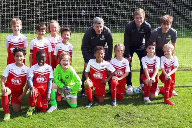 Gruppenfoto einer Jugendfu&szlig;ballmannschaft in roten Trikots, stehend und kniend vor einem Tor auf dem Rasenplatz.