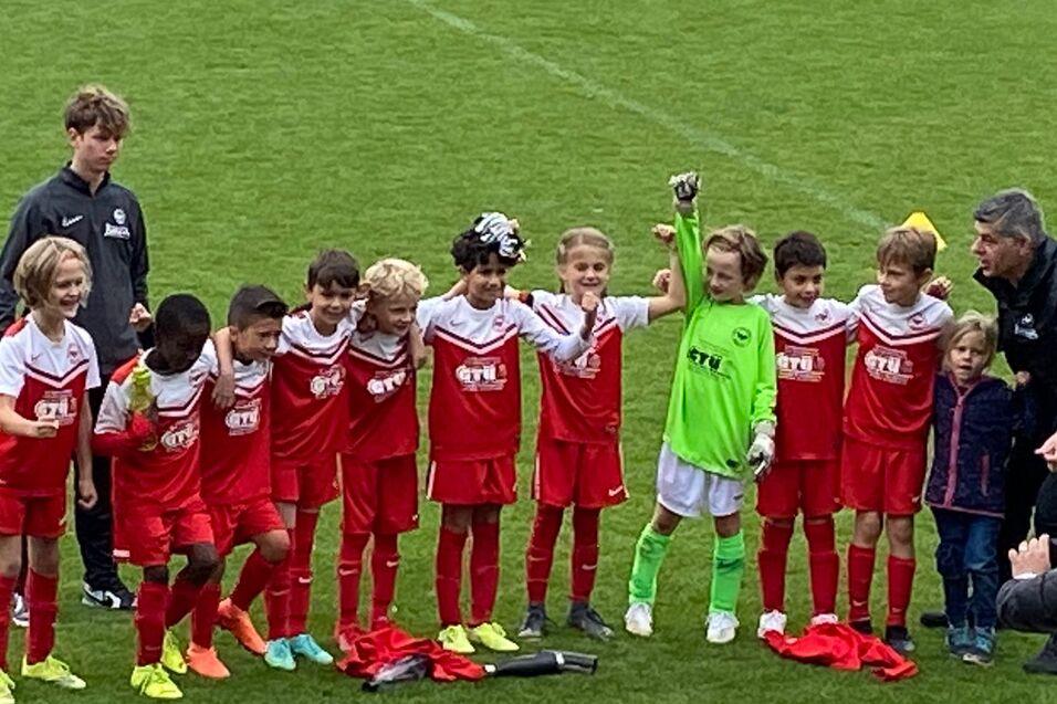 Mannschaft von jungen Fu&szlig;ballspielern in roten Trikots posiert auf dem Spielfeld nach einem Spiel.