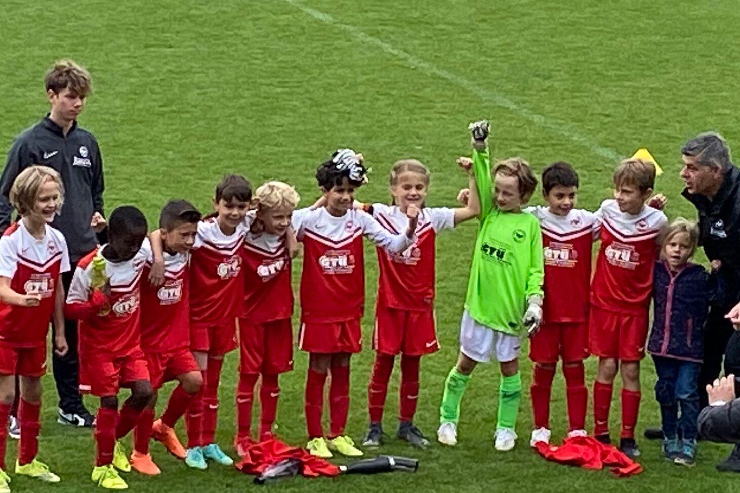Mannschaft von jungen Fu&szlig;ballspielern in roten Trikots posiert auf dem Spielfeld nach einem Spiel.