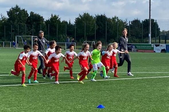 Gruppe von Kindern in roter Sportkleidung beim Lauftraining auf einem k&uuml;nstlichen Fu&szlig;ballplatz.