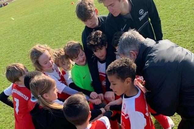 Gruppierung von Kindern in Fu&szlig;balltrikots um einen Trainer, w&auml;hrend sie sich zum Team-Motivationsruf versammeln.