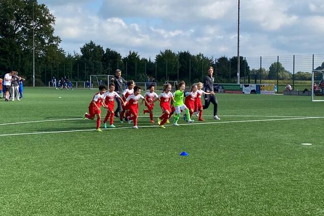 Gruppe von Kindern in roter Sportkleidung beim Lauftraining auf einem k&uuml;nstlichen Fu&szlig;ballplatz.