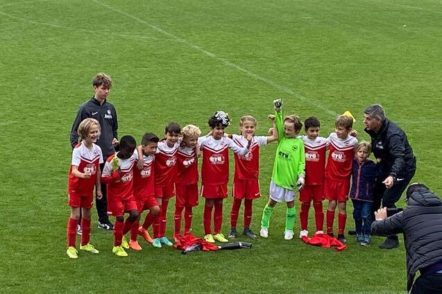 Mannschaft von jungen Fu&szlig;ballspielern in roten Trikots posiert auf dem Spielfeld nach einem Spiel.
