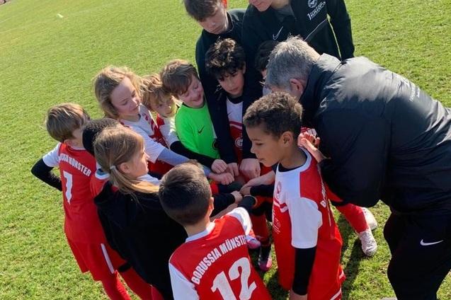 Gruppierung von Kindern in Fu&szlig;balltrikots um einen Trainer, w&auml;hrend sie sich zum Team-Motivationsruf versammeln.