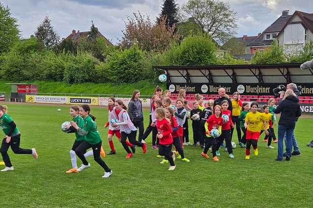Gruppierung von Kindern in Sportkleidung, die enthusiastisch auf einem Fu&szlig;ballplatz mit B&auml;llen in unterschiedlichen Positionen laufen.