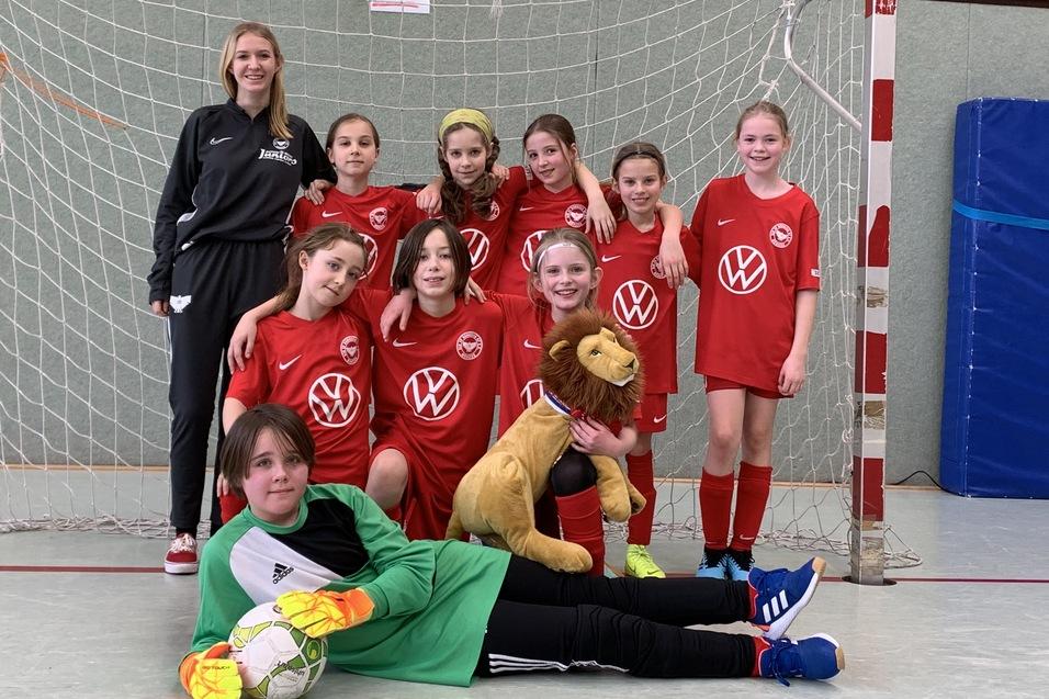 Gruppe von M&auml;dchen in roten Fu&szlig;balltrikots steht vor einem Tor, eine M&auml;dchen tr&auml;gt ein L&ouml;wenkost&uuml;m, torwart liegt im Vordergrund.