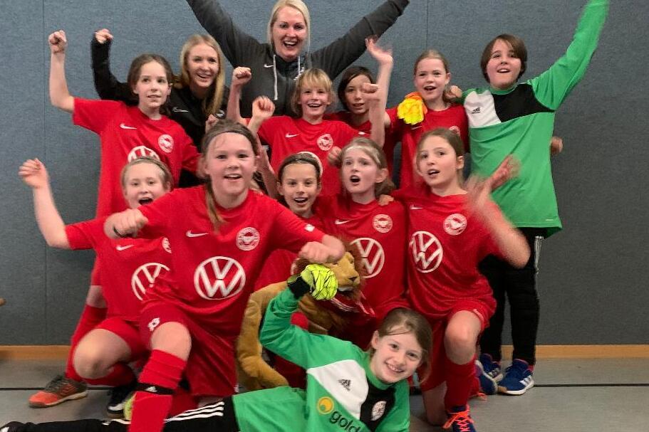 M&auml;dchenfu&szlig;ballmannschaft in roten Trikots posiert fr&ouml;hlich nach dem Spiel, einige halten Torwarthandschuhe und feiern.