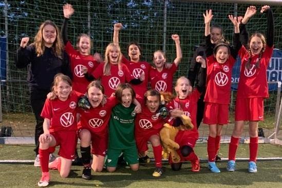 Gruppenselfie von M&auml;dchenfu&szlig;ballspielerinnen in roten Trikots, zufriedene Gesichter, Jubel vor dem Tor.