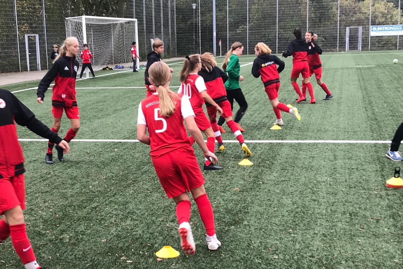 M&auml;dchenfu&szlig;ballmannschaft in roten Trikots trainiert auf einem Kunstrasenplatz mit H&uuml;tchen als Markierungen.