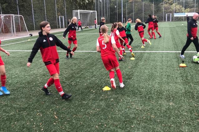 M&auml;dchenfu&szlig;ballmannschaft in roten Trikots trainiert auf einem Kunstrasenplatz mit H&uuml;tchen als Markierungen.