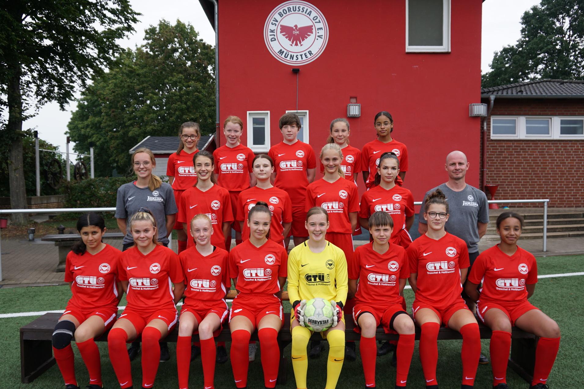 Mannschaftsfoto einer M&auml;dchenfu&szlig;ballmannschaft in roten Trikots vor einem Vereinsgeb&auml;ude.