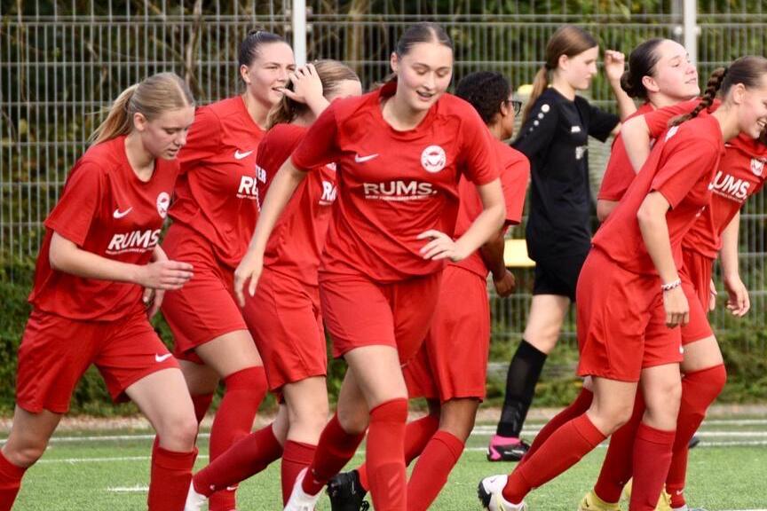 Mannschaft von Frauen in roten Trikots beim Aufw&auml;rmen auf einem Fu&szlig;ballfeld.