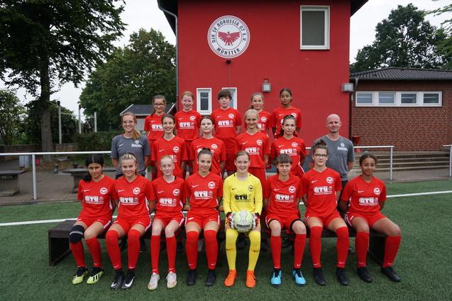 Mannschaftsfoto einer M&auml;dchenfu&szlig;ballmannschaft in roten Trikots vor einem Vereinsgeb&auml;ude.