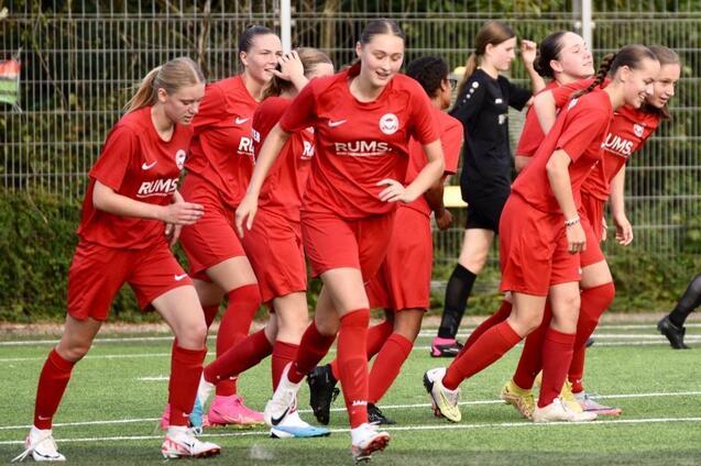 Mannschaft von Frauen in roten Trikots beim Aufw&auml;rmen auf einem Fu&szlig;ballfeld.