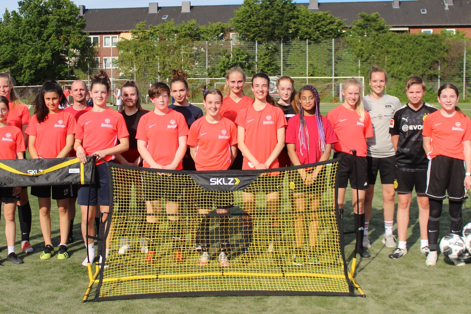 Gruppe von Fu&szlig;ballspielerinnen in roten Trikots steht vor einem Tor auf einem gr&uuml;nen Sportplatz.