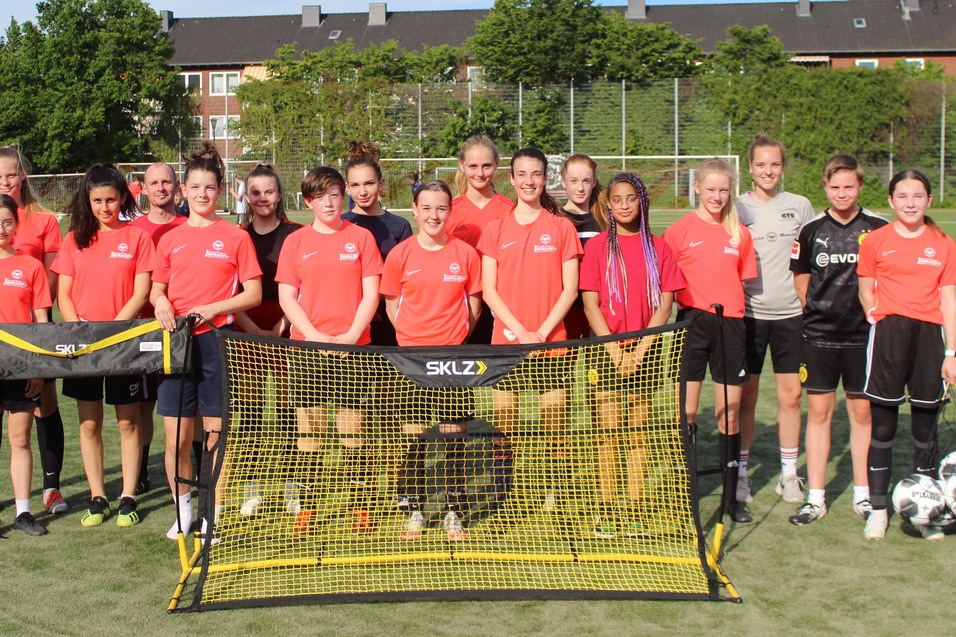 Gruppe von Fu&szlig;ballspielerinnen in roten Trikots steht vor einem Tor auf einem gr&uuml;nen Sportplatz.