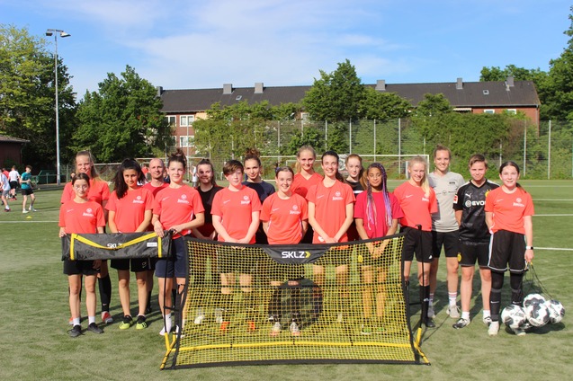 Gruppe von Fu&szlig;ballspielerinnen in roten Trikots steht vor einem Tor auf einem gr&uuml;nen Sportplatz.