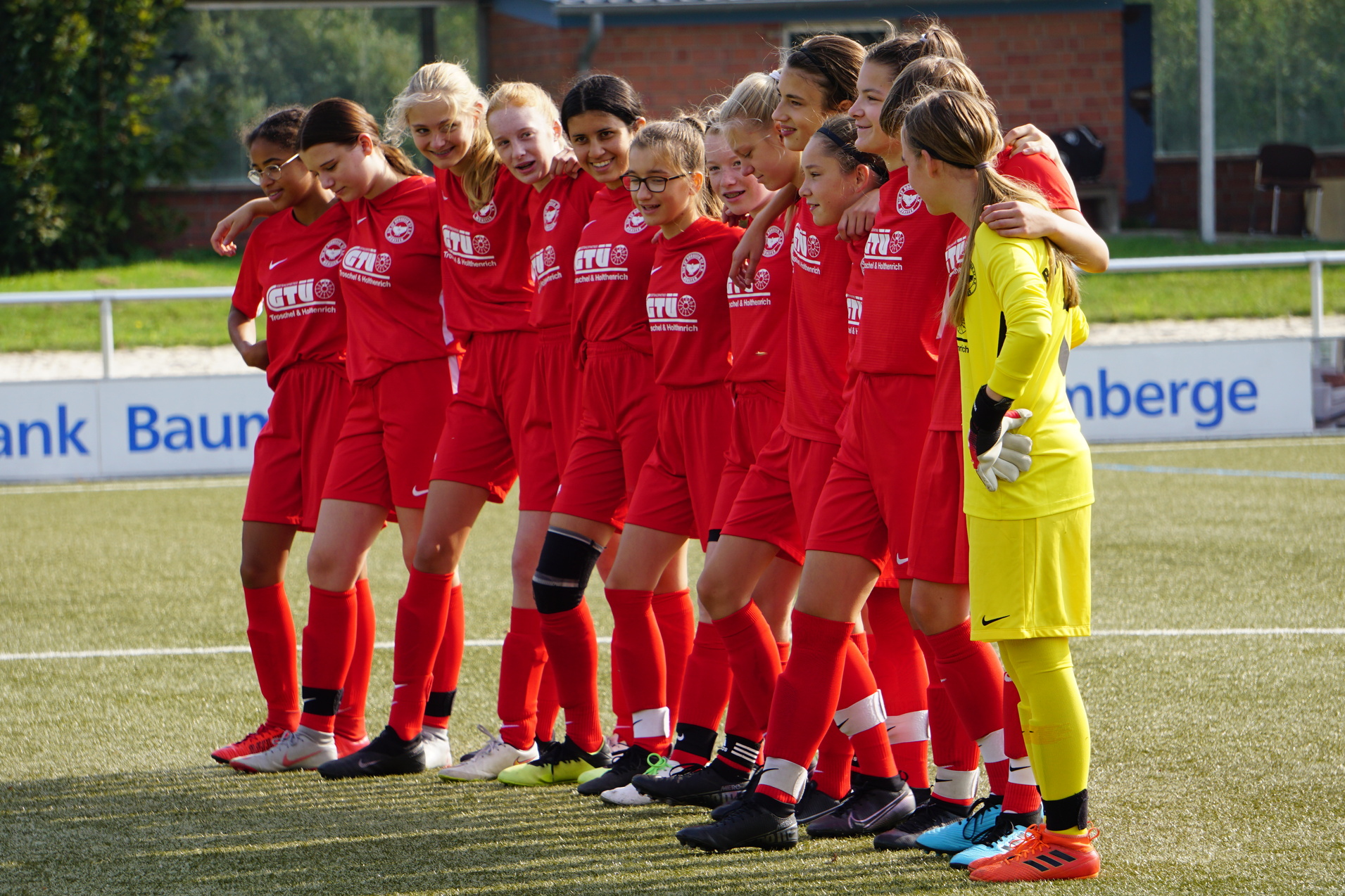 Eine Fu&szlig;ballmannschaft von M&auml;dchen in roten Trikots steht auf dem Platz, bereit f&uuml;r ein Spiel.