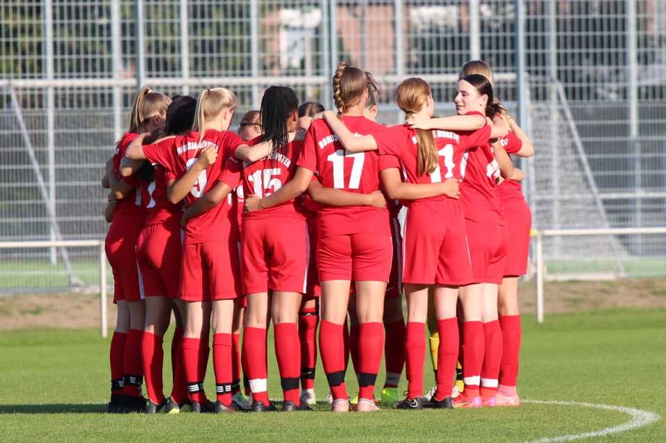Frauenfu&szlig;ballmannschaft in roten Trikots umarmt sich auf dem Spielfeld vor dem Spiel.