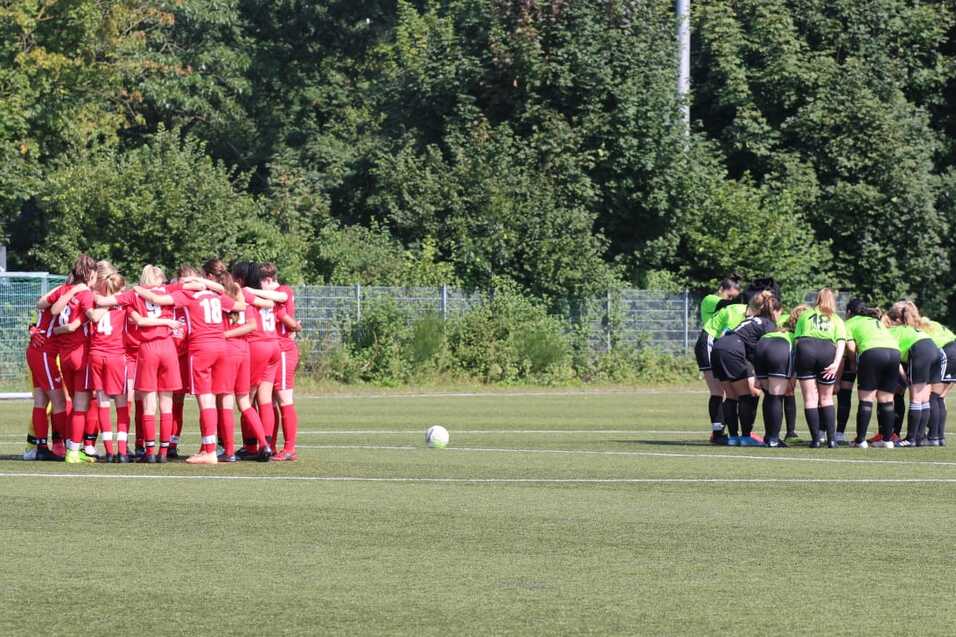 Zwei Gruppen von Fu&szlig;ballspielern in roten und gr&uuml;nen Trikots versammeln sich zum Teamgespr&auml;ch auf einem Sportplatz.