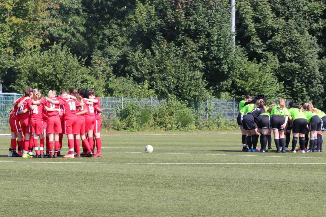 Zwei Gruppen von Fu&szlig;ballspielern in roten und gr&uuml;nen Trikots versammeln sich zum Teamgespr&auml;ch auf einem Sportplatz.