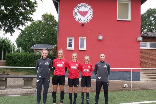 F&uuml;nf Fu&szlig;ballspielerinnen in roten Trikots stehen vor einem Vereinsgeb&auml;ude mit Logo des SV Borussia M&uuml;nster.
