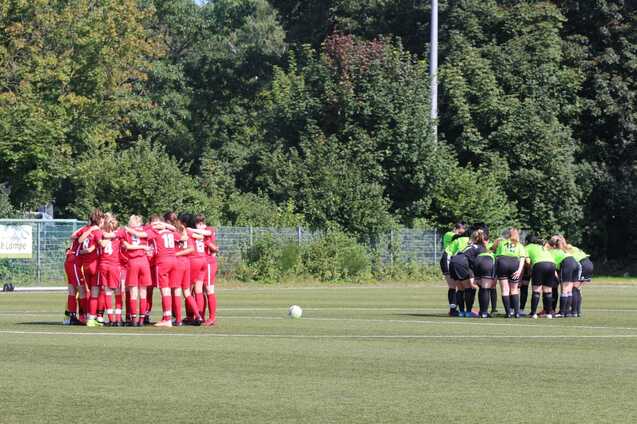 Zwei Gruppen von Fu&szlig;ballspielern in roten und gr&uuml;nen Trikots versammeln sich zum Teamgespr&auml;ch auf einem Sportplatz.